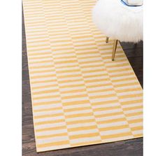 a yellow and white rug on a wooden floor with a chair in the corner next to it