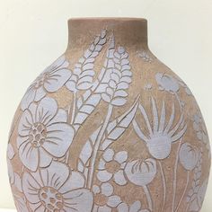 a brown vase with white flowers and leaves painted on the side, sitting on a table