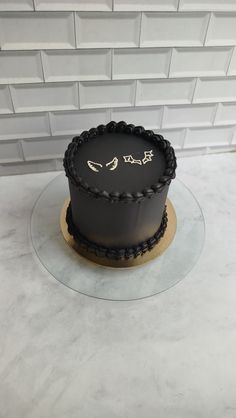 a black cake sitting on top of a glass plate next to a white brick wall