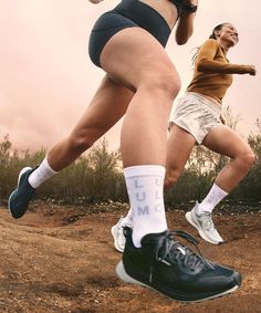 two women are running in the dirt with their shoes on and one has her leg up