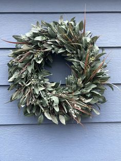 a wreath hanging on the side of a blue building with green leaves and branches around it