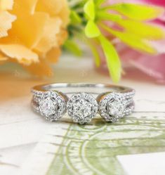 three stone diamond ring sitting on top of a table next to a bouquet of flowers