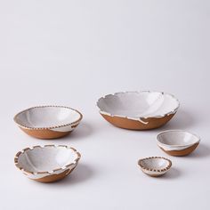 three bowls and two spoons on a white surface, one with brown trim around the edge