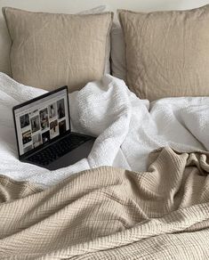 an open laptop computer sitting on top of a bed covered in white sheets and pillows