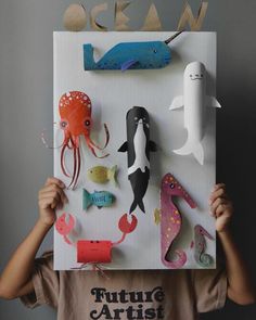 a young boy holding up a paper cutout with sea animals and fish on it