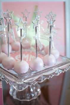 there are some cake pops on a glass plate with pink frosting and silver decorations