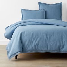 a bed with blue sheets and pillows on top of wooden flooring in front of a white wall