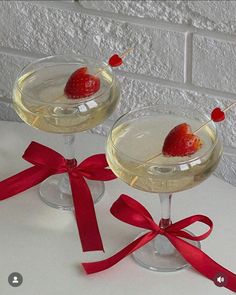 two wine glasses with strawberries in them and red ribbon on the rim, sitting next to each other