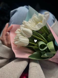 a bouquet of white tulips is wrapped in pink paper and held by someone's hand