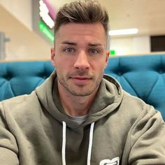 a man in a grey hoodie is sitting on a blue couch and looking at the camera