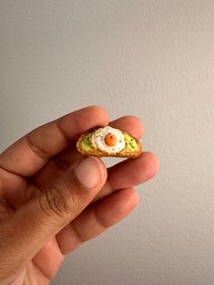 a hand holding a tiny egg and avocado sandwich on it's fingers