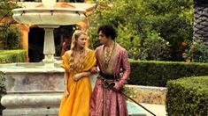 a man and woman dressed in medieval clothing standing next to each other near a fountain