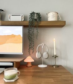 a computer monitor sitting on top of a wooden desk next to a cup and candle