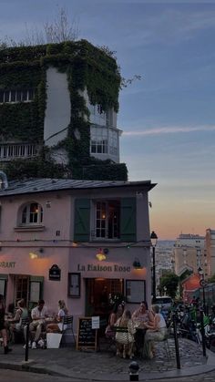 people are sitting outside in front of a building with plants growing on the side of it