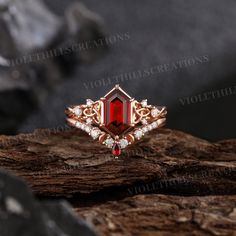 a red stone surrounded by white diamonds sits on top of a piece of drift wood