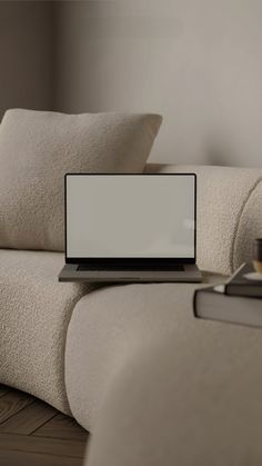 a laptop computer sitting on top of a white couch next to pillows and a cup