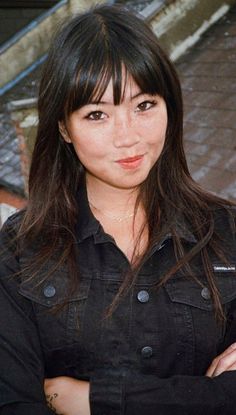 a woman standing with her arms crossed and looking at the camera while wearing a black shirt