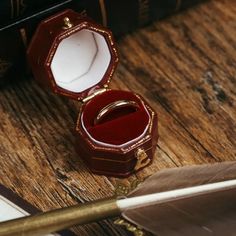 an open ring box sitting on top of a wooden table next to a feather quill