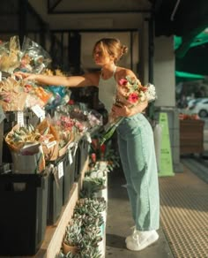 a woman standing in front of a store filled with lots of flowers and other items