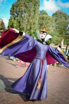 a woman in a purple dress and crown with her arms spread out, posing for the camera