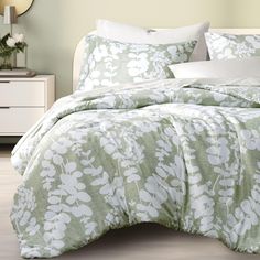 a bed with green and white comforters in a bedroom next to a mirror on the wall