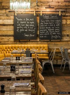 the interior of a restaurant with wooden tables and yellow leather booths, chalkboard menus on the wall