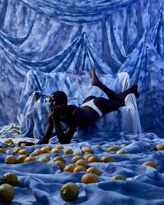 a man laying on top of a bed covered in lemons next to a blue curtain