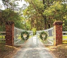 a white gate with wreaths on it and two gates leading into the distance are surrounded by trees