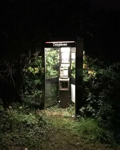 an old phone booth sitting in the middle of a forest at night with its door open