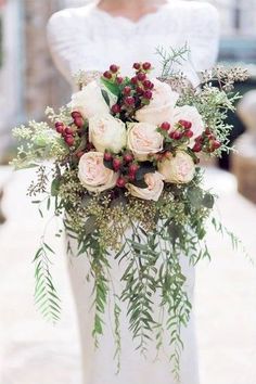 a woman in white dress holding a bouquet of flowers with greenery on the bottom