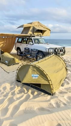 an suv is parked on the beach next to two tents and chairs, while another van sits in the background