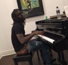 a man sitting at a black piano in front of a painting on the wall behind him