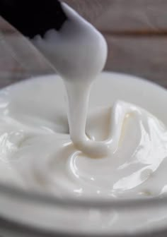 a spoon is pouring white cream into a bowl