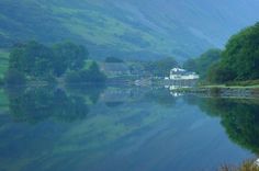 a body of water surrounded by mountains and trees with houses on the shore in the distance