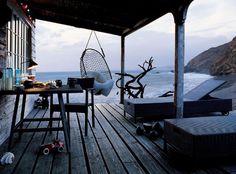 an outdoor deck with chairs, table and hammock hanging from the roof over looking the ocean