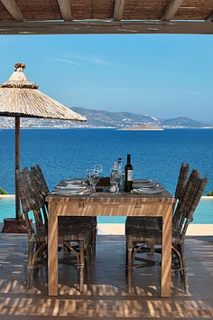 an outdoor dining table with chairs and umbrella overlooking the ocean