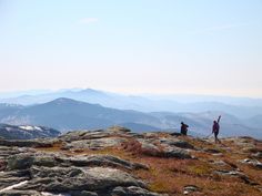 two people standing on top of a mountain with their arms in the air and mountains in the background