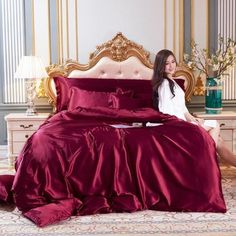 a woman sitting on top of a bed next to a red comforter and pillows