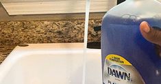 a hand that is holding a bottle of dawn liquid in front of a sink with granite counter tops