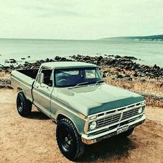 an old pick up truck parked on the side of a road next to the ocean