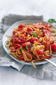 a plate of spaghetti with tomatoes and basil on the side, ready to be eaten