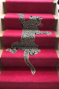 the cat is sitting on top of the red carpeted stair treads, which are decorated with black and white leopard prints