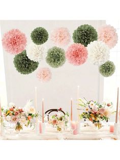 a table topped with lots of flowers and candles next to a wall covered in paper pom poms