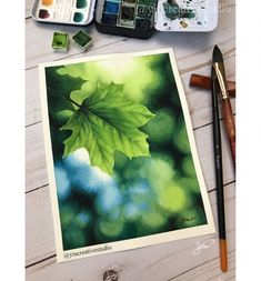 an art project with watercolors and paintbrushes on a table next to a leaf