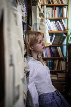 a woman with glasses sitting in front of a bookshelf filled with lots of books