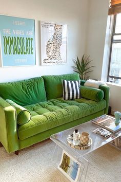 a green couch sitting in front of a window next to a coffee table and lamp