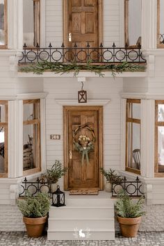 a white house with two potted plants on the front porch and a wooden door