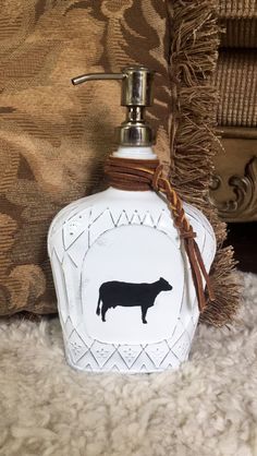 a white bottle with a black cow on it sitting next to a brown pillow and rug