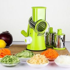 a green juicer sitting on top of a wooden cutting board next to bowls of vegetables