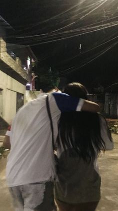 two people walking down the street at night with their arms around each other's backs